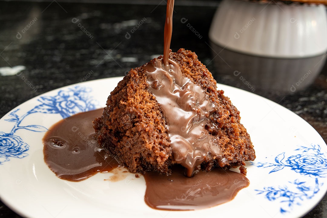 Derramando calda de chocolate em uma fatia de bolo de chocolate sobre um fundo escuro de mármore