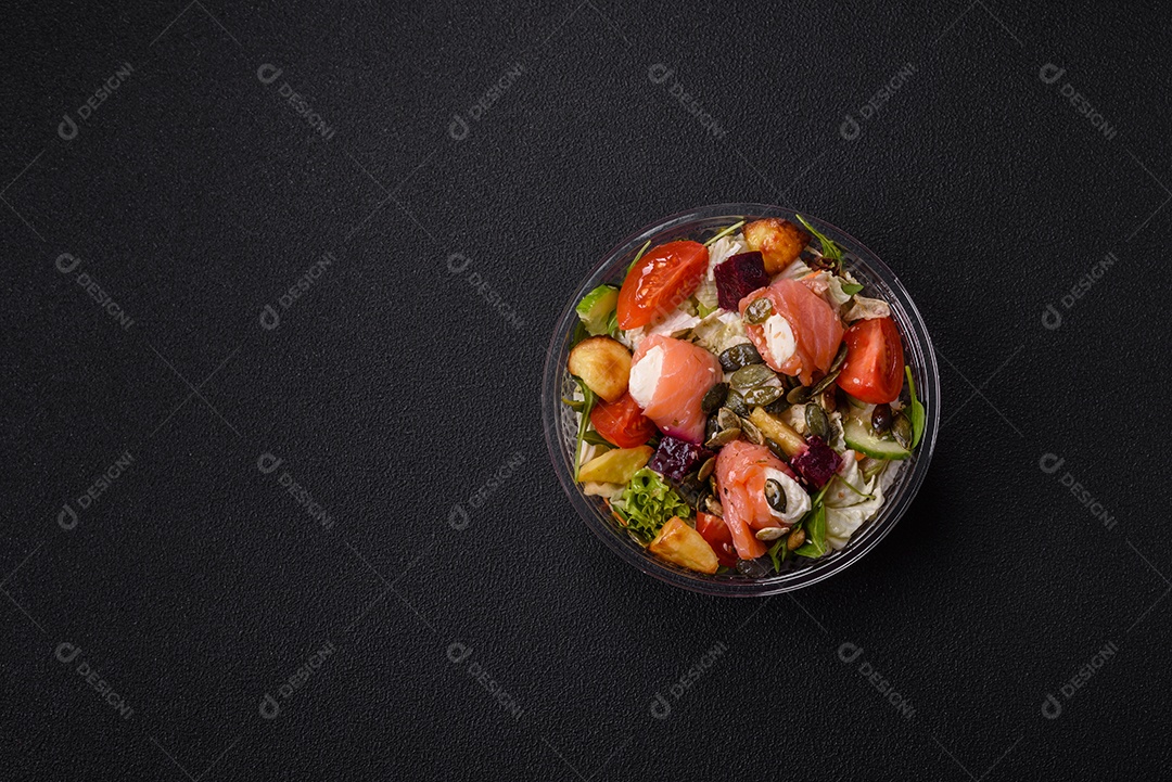 Deliciosa salada suculenta com salmão, tomate, pepino, ervas, sementes de abóbora, sal e especiarias em uma placa cerâmica sobre um fundo escuro de concreto