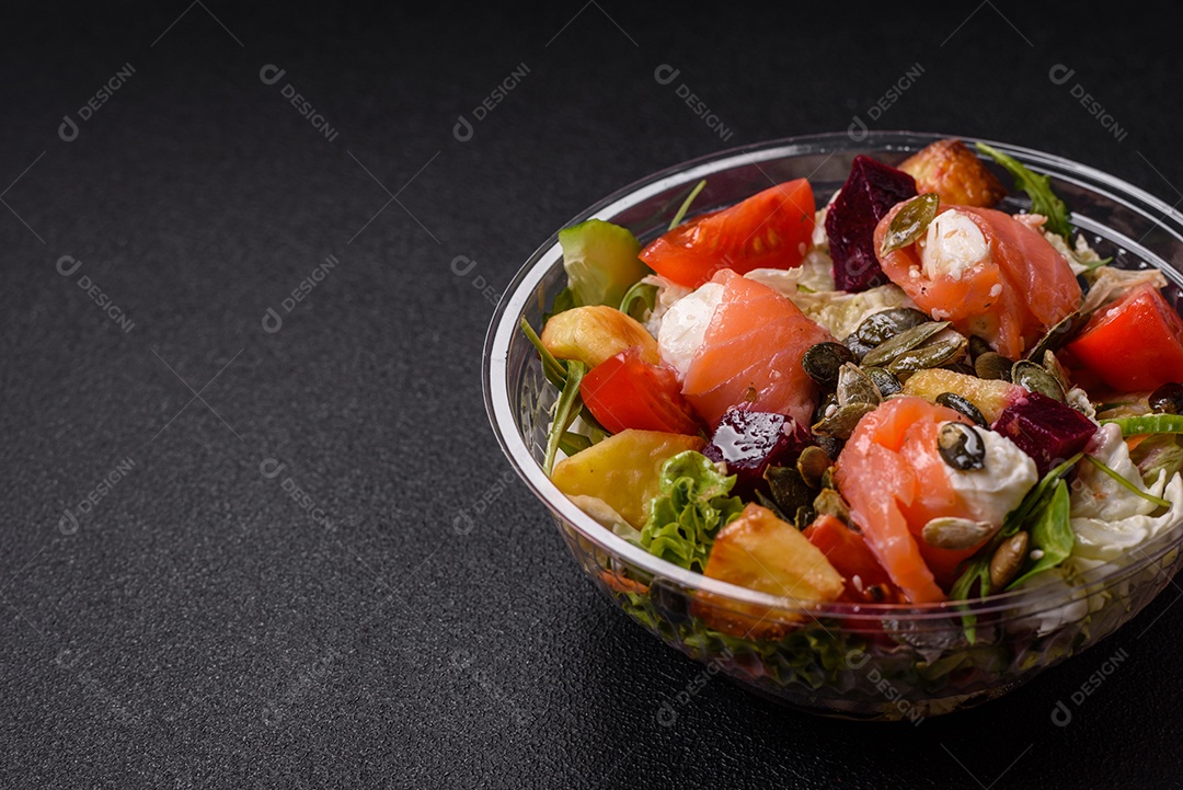 Deliciosa salada suculenta com salmão, tomate, pepino, ervas, sementes de abóbora, sal e especiarias em uma placa cerâmica sobre um fundo escuro de concreto