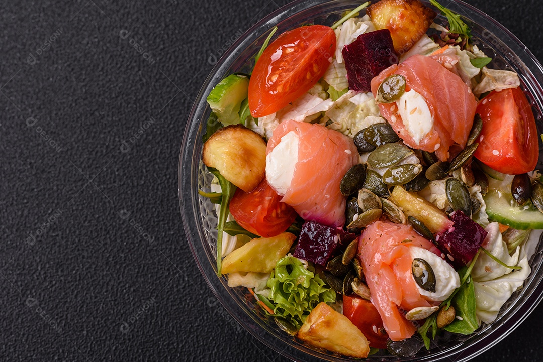 Deliciosa salada suculenta com salmão, tomate, pepino, ervas, sementes de abóbora, sal e especiarias em uma placa cerâmica sobre um fundo escuro de concreto