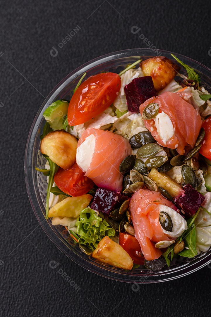 Deliciosa salada suculenta com salmão, tomate, pepino, ervas, sementes de abóbora, sal e especiarias em uma placa cerâmica sobre um fundo escuro de concreto