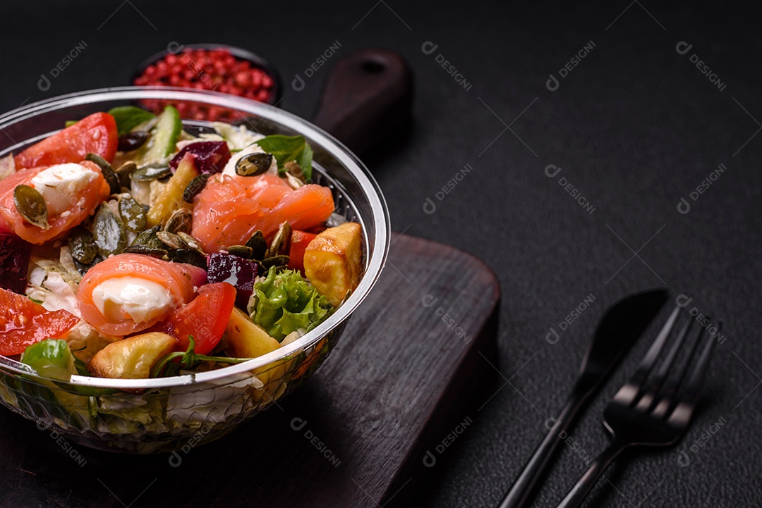 Deliciosa salada suculenta com salmão, tomate, pepino, ervas, sementes de abóbora, sal e especiarias em uma placa cerâmica sobre um fundo escuro de concreto