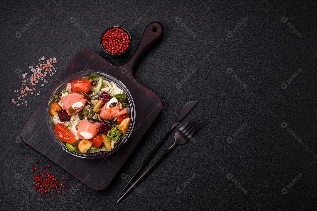 Deliciosa salada suculenta com salmão, tomate, pepino, ervas, sementes de abóbora, sal e especiarias em uma placa cerâmica sobre um fundo escuro de concreto