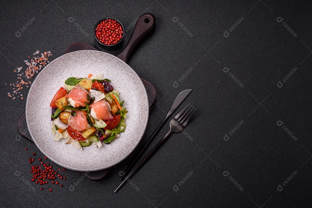 Deliciosa salada suculenta com salmão, tomate, pepino, ervas, sementes de abóbora, sal e especiarias em uma placa cerâmica sobre um fundo escuro de concreto