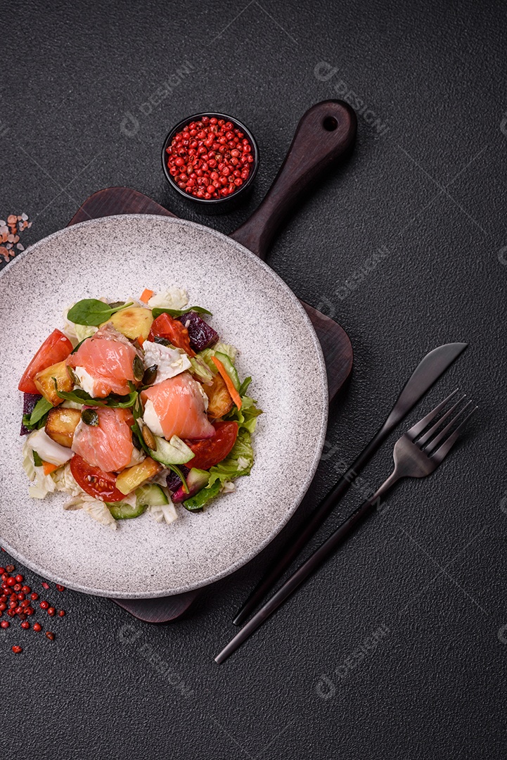 Deliciosa salada suculenta com salmão, tomate, pepino, ervas, sementes de abóbora, sal e especiarias em uma placa cerâmica sobre um fundo escuro de concreto