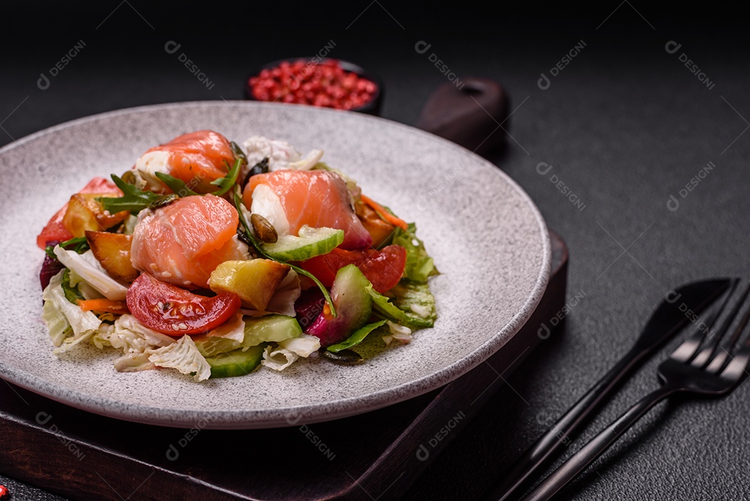 Deliciosa salada suculenta com salmão, tomate, pepino, ervas, sementes de abóbora, sal e especiarias em uma placa cerâmica sobre um fundo escuro de concreto