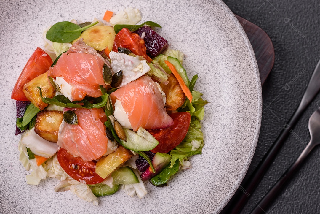 Deliciosa salada suculenta com salmão, tomate, pepino, ervas, sementes de abóbora, sal e especiarias em uma placa cerâmica sobre um fundo escuro de concreto