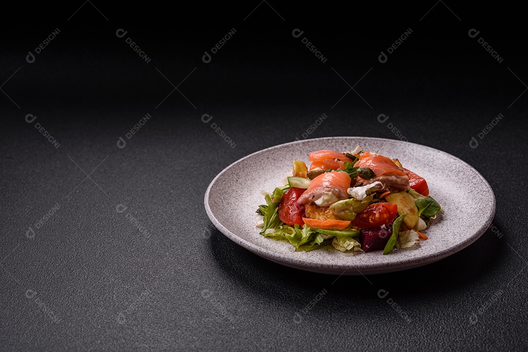 Deliciosa salada suculenta com salmão, tomate, pepino, ervas, sementes de abóbora, sal e especiarias em uma placa cerâmica sobre um fundo escuro de concreto