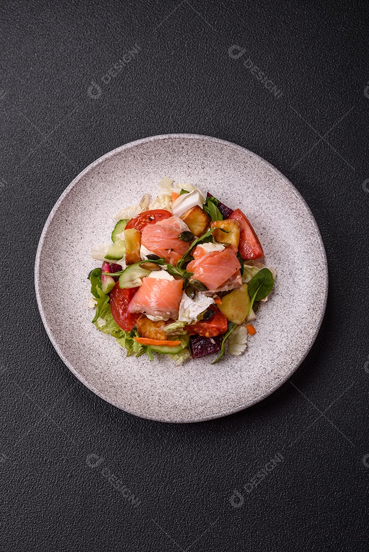 Deliciosa salada suculenta com salmão, tomate, pepino, ervas, sementes de abóbora, sal e especiarias em uma placa cerâmica sobre um fundo escuro de concreto