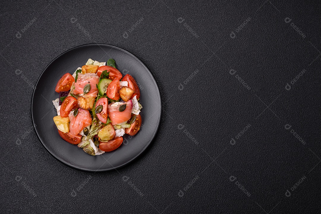 Deliciosa salada suculenta com salmão, tomate, pepino, ervas, sementes de abóbora, sal e especiarias em uma placa cerâmica sobre um fundo escuro de concreto