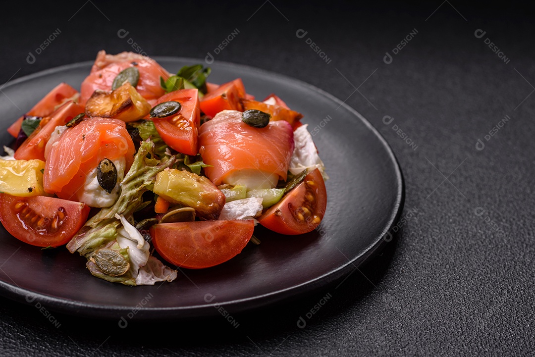 Deliciosa salada suculenta com salmão, tomate, pepino, ervas, sementes de abóbora, sal e especiarias em uma placa cerâmica sobre um fundo escuro de concreto