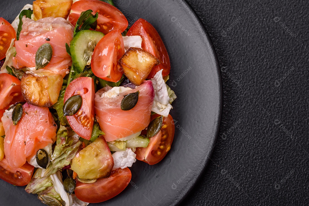 Deliciosa salada suculenta com salmão, tomate, pepino, ervas, sementes de abóbora, sal e especiarias em uma placa cerâmica sobre um fundo escuro de concreto