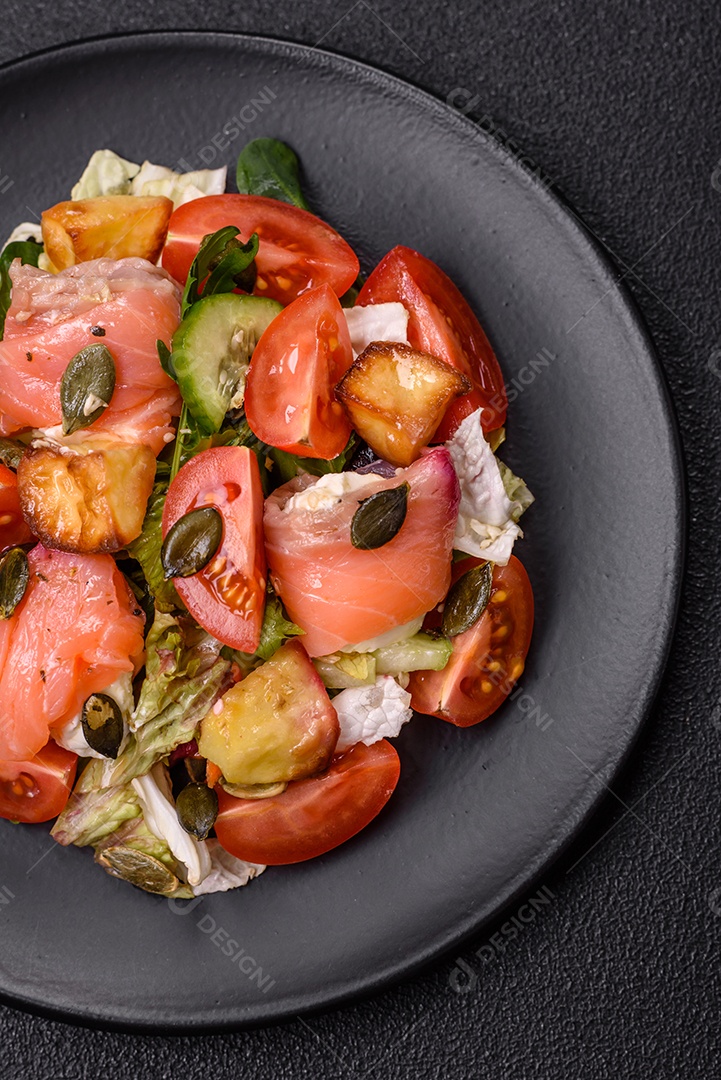 Deliciosa salada suculenta com salmão, tomate, pepino, ervas, sementes de abóbora, sal e especiarias em uma placa cerâmica sobre um fundo escuro de concreto