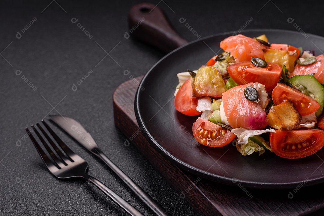 Deliciosa salada suculenta com salmão, tomate, pepino, ervas, sementes de abóbora, sal e especiarias em uma placa cerâmica sobre um fundo escuro de concreto
