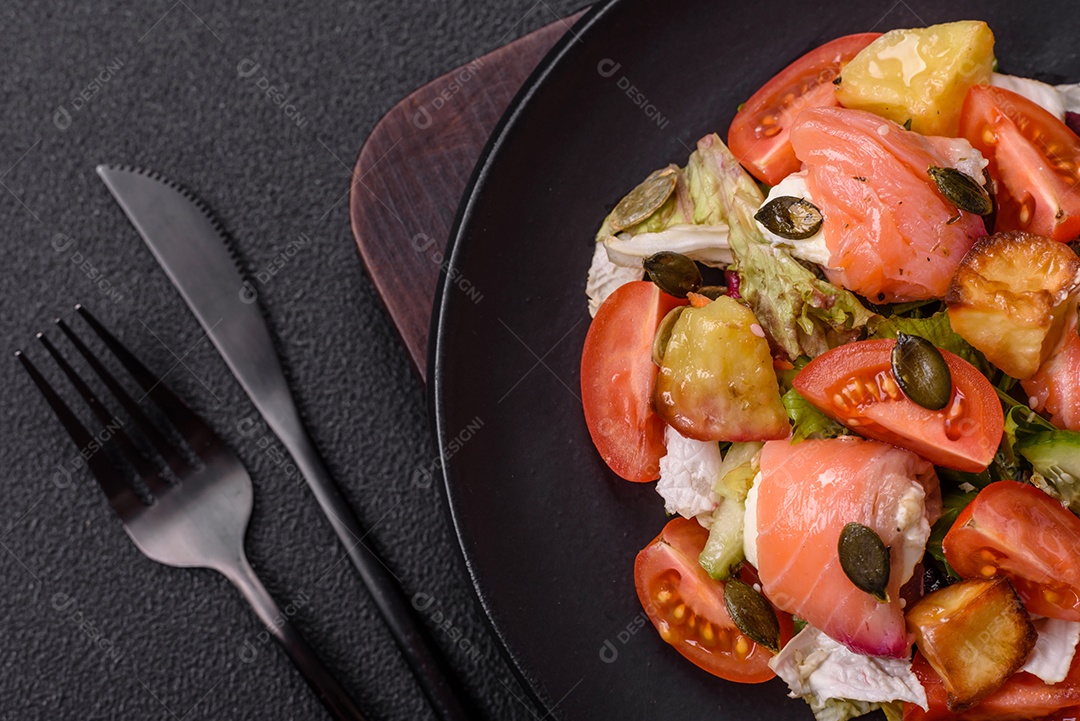 Deliciosa salada suculenta com salmão, tomate, pepino, ervas, sementes de abóbora, sal e especiarias em uma placa cerâmica sobre um fundo escuro de concreto