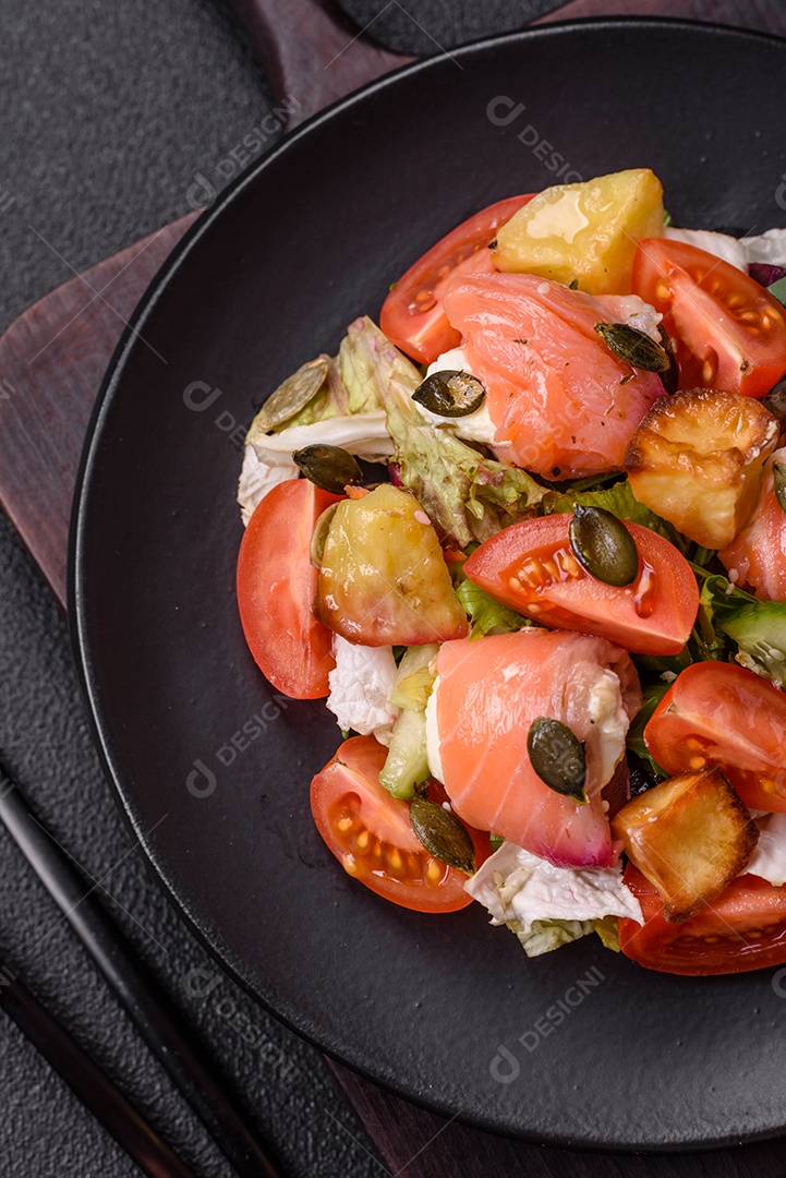 Deliciosa salada suculenta com salmão, tomate, pepino, ervas, sementes de abóbora, sal e especiarias em uma placa cerâmica sobre um fundo escuro de concreto