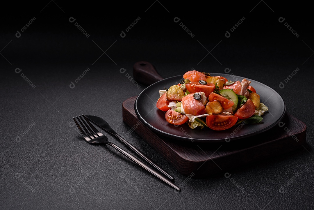 Deliciosa salada suculenta com salmão, tomate, pepino, ervas, sementes de abóbora, sal e especiarias em uma placa cerâmica sobre um fundo escuro de concreto