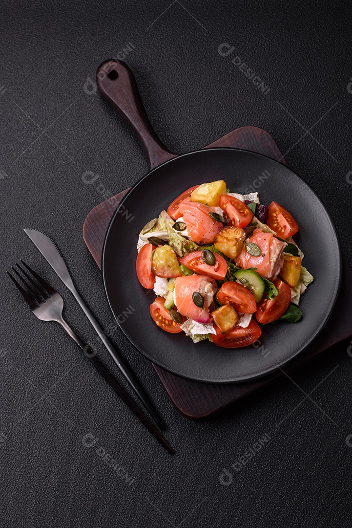 Deliciosa salada suculenta com salmão, tomate, pepino, ervas, sementes de abóbora, sal e especiarias em uma placa cerâmica sobre um fundo escuro de concreto