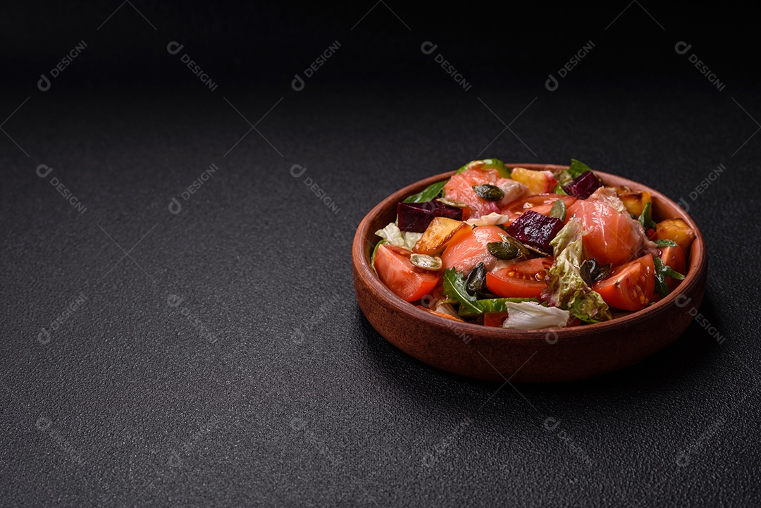 Deliciosa salada suculenta com salmão, tomate, pepino, ervas, sementes de abóbora, sal e especiarias em uma placa cerâmica sobre um fundo escuro de concreto