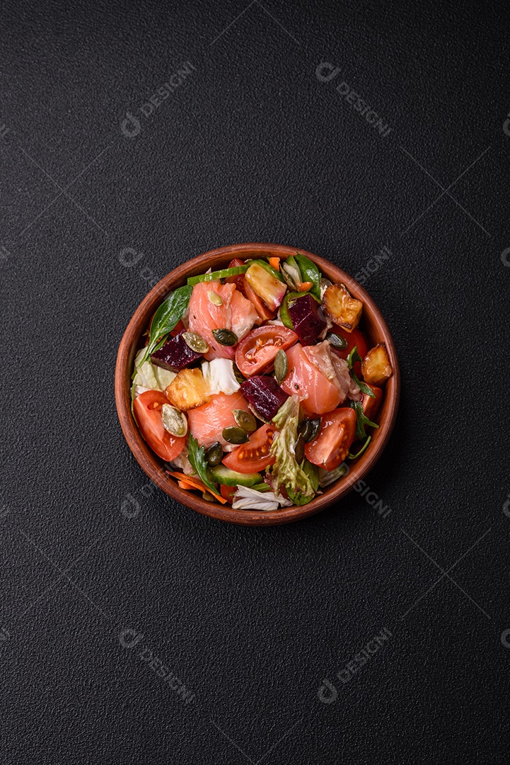 Deliciosa salada suculenta com salmão, tomate, pepino, ervas, sementes de abóbora, sal e especiarias em uma placa cerâmica sobre um fundo escuro de concreto