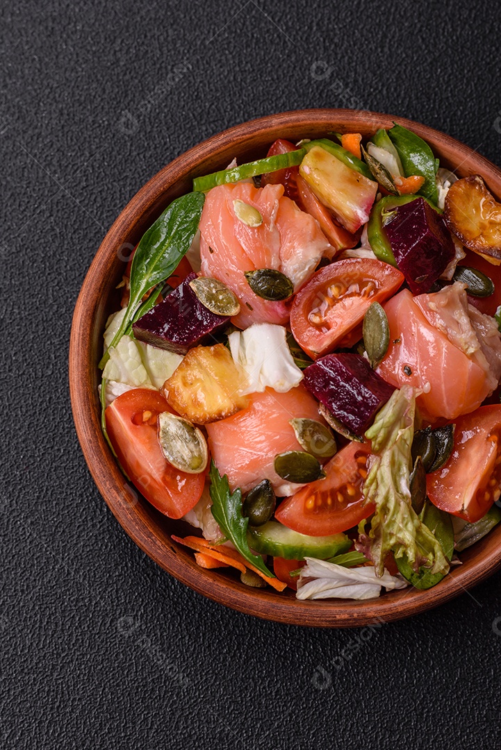 Deliciosa salada suculenta com salmão, tomate, pepino, ervas, sementes de abóbora, sal e especiarias em uma placa cerâmica sobre um fundo escuro de concreto
