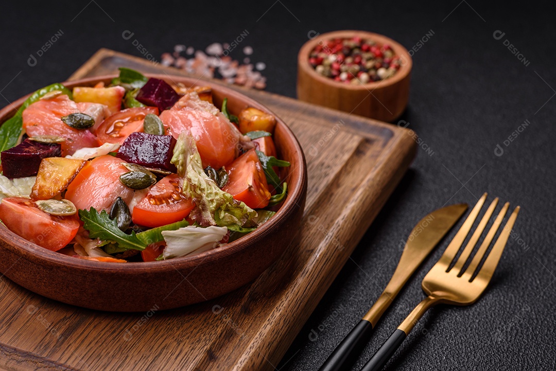Deliciosa salada suculenta com salmão, tomate, pepino, ervas, sementes de abóbora, sal e especiarias em uma placa cerâmica sobre um fundo escuro de concreto