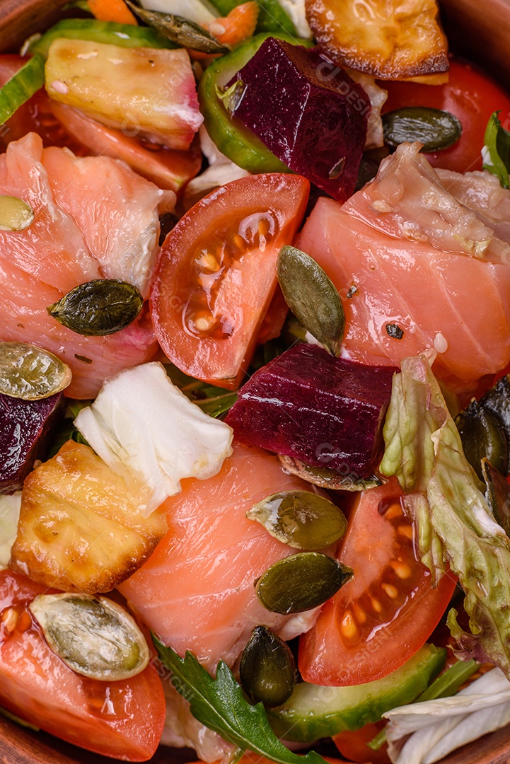 Deliciosa salada suculenta com salmão, tomate, pepino, ervas, sementes de abóbora, sal e especiarias em uma placa cerâmica sobre um fundo escuro de concreto