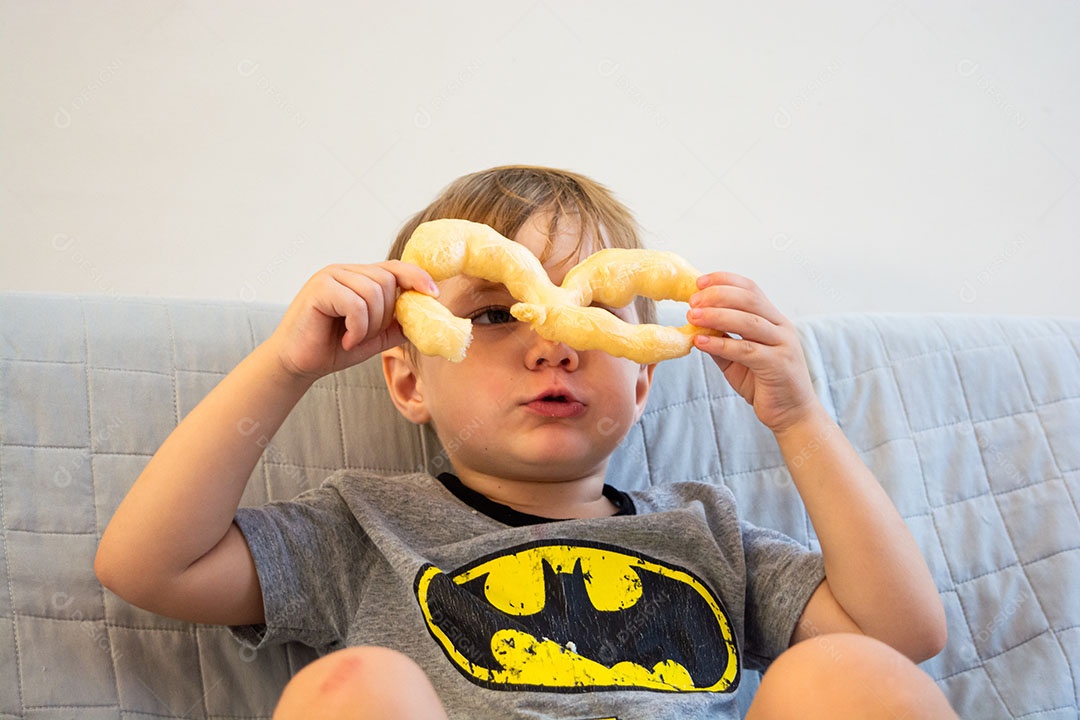 Criança sentada no sofá comendo biscoito de polvilho.