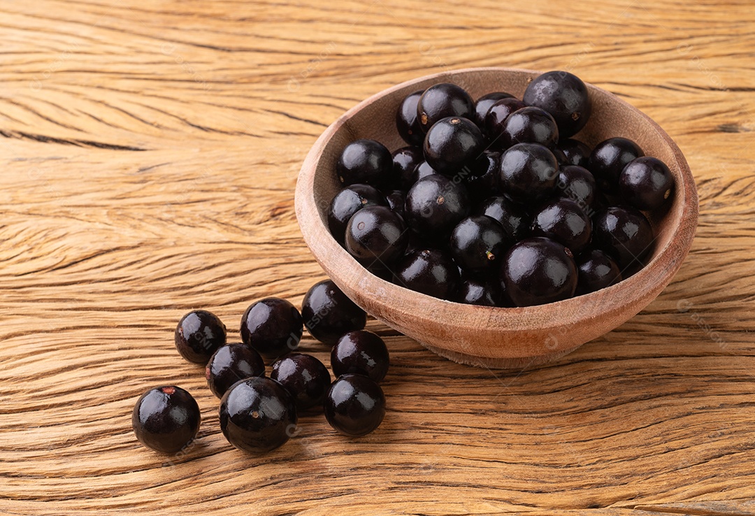 Tigela redonda com frutos da jabuticaba dentro sobre fundo de madeira