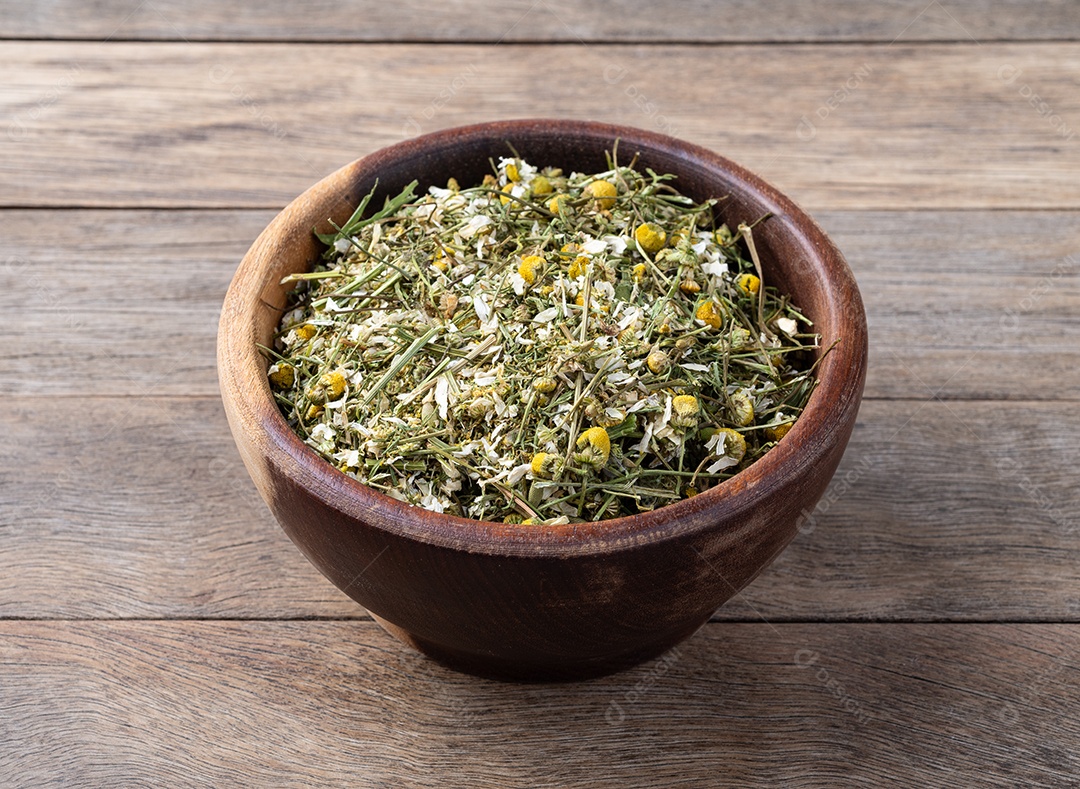 Camomila em folhas e flor dentro da tigela sobre fundo de madeira