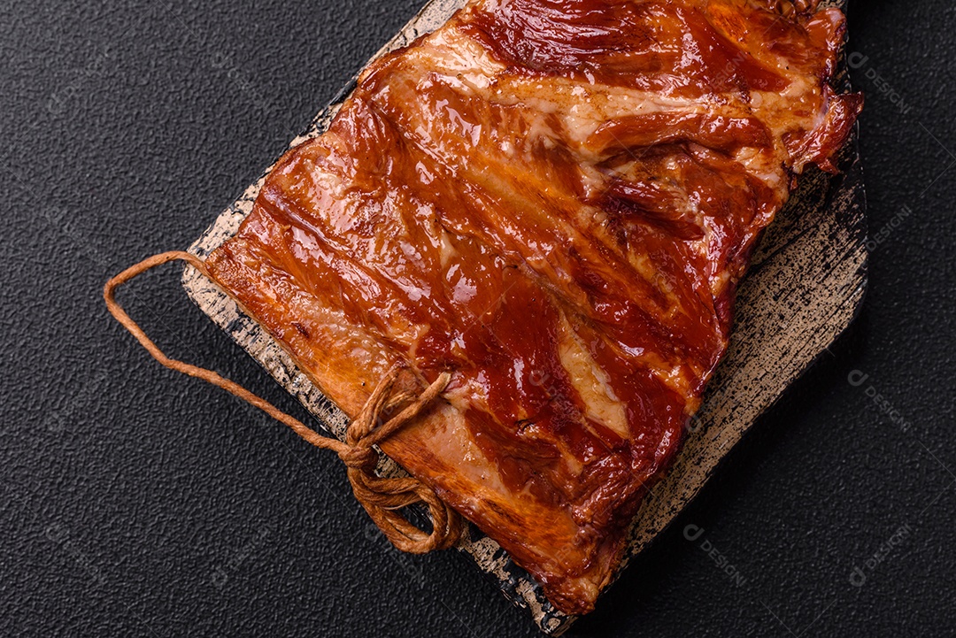 Deliciosas costelas defumadas ou grelhadas com azeitonas, especiarias e ervas sobre fundo escuro de concreto