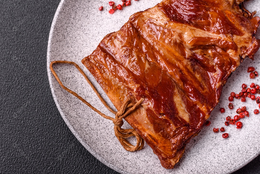 Deliciosas costelas defumadas ou grelhadas com azeitonas, especiarias e ervas sobre fundo escuro de concreto