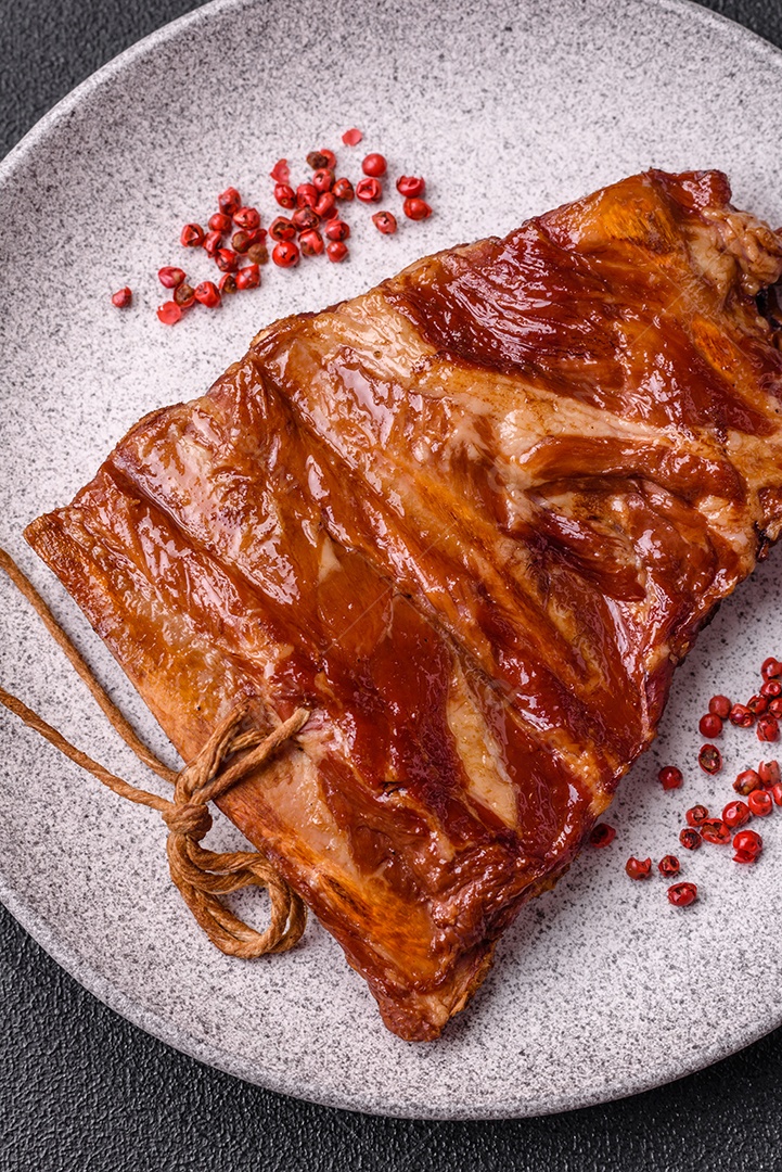 Deliciosas costelas defumadas ou grelhadas com azeitonas, especiarias e ervas sobre fundo escuro de concreto