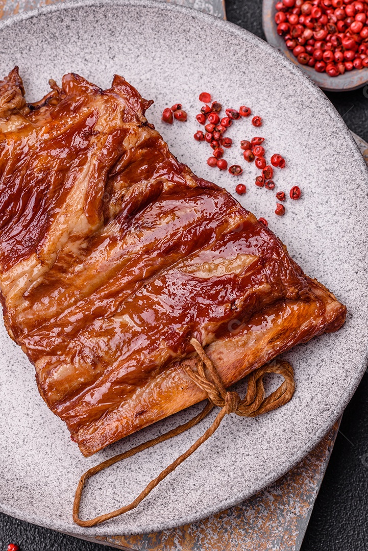 Deliciosas costelas defumadas ou grelhadas com azeitonas, especiarias e ervas sobre fundo escuro de concreto