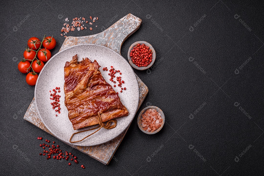 Deliciosas costelas defumadas ou grelhadas com azeitonas, especiarias e ervas sobre fundo escuro de concreto