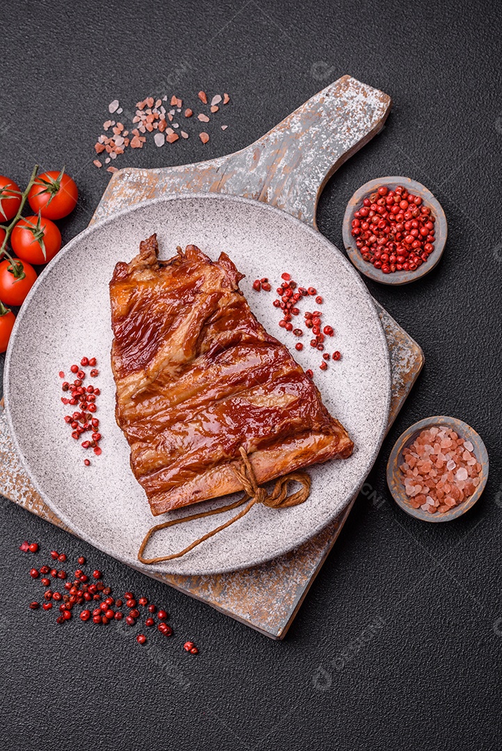 Deliciosas costelas defumadas ou grelhadas com azeitonas, especiarias e ervas sobre fundo escuro de concreto