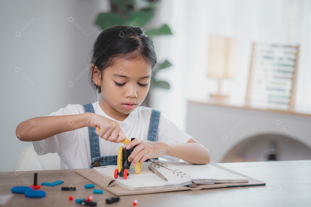 Uma criança está sentada à mesa com um livro e tentando montar um carrinho