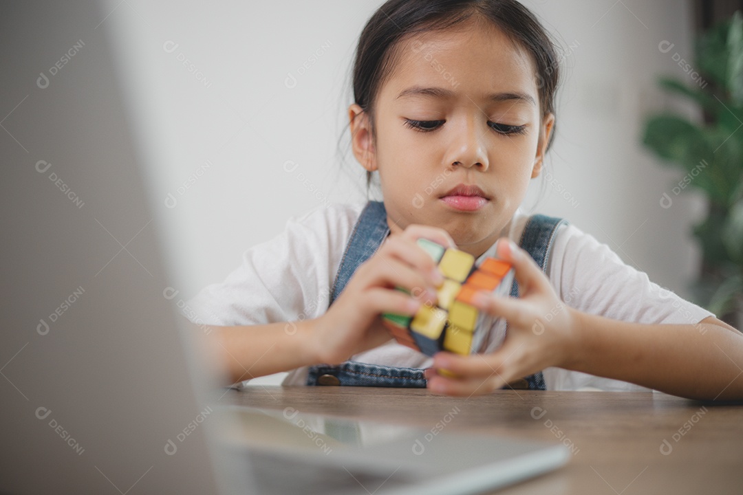 Uma menina está sentada à mesa com um cubo de Rubik na mão