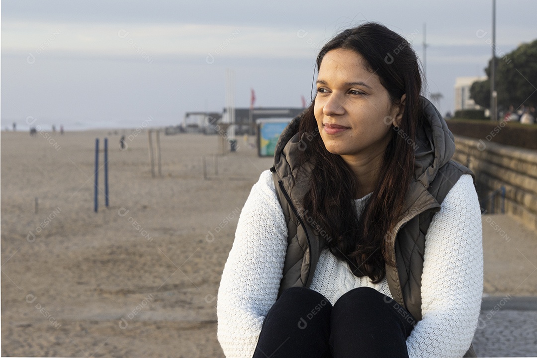 Mulher sentada olhando para o mar em uma praia