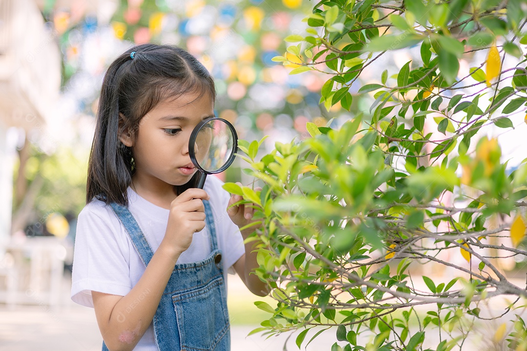 Uma garotinha olhando através de uma lupa para uma folha