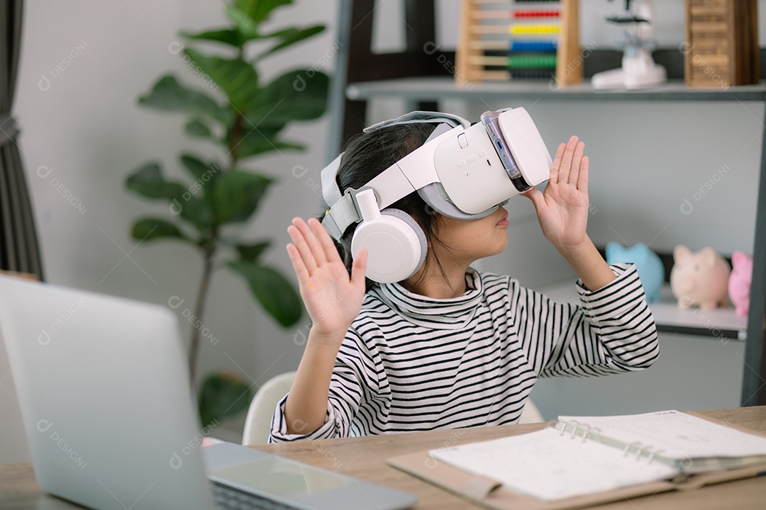 Menina asiática usando óculos VR com um laptopcolocado sobre a mesa