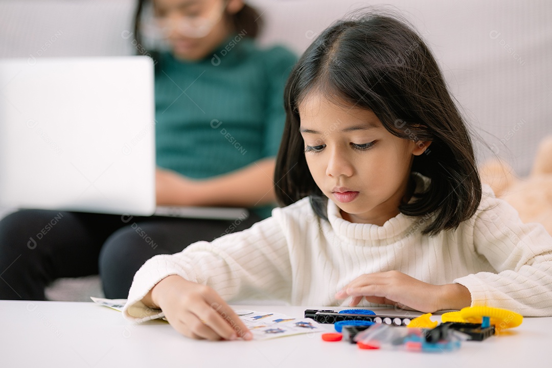 Uma criança brincando com legos e sua irmã acessando ao laptop