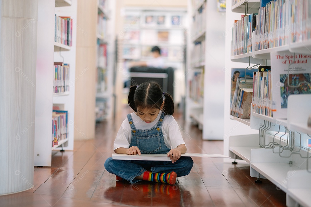 Little girl sitting on the ground reading book in a library