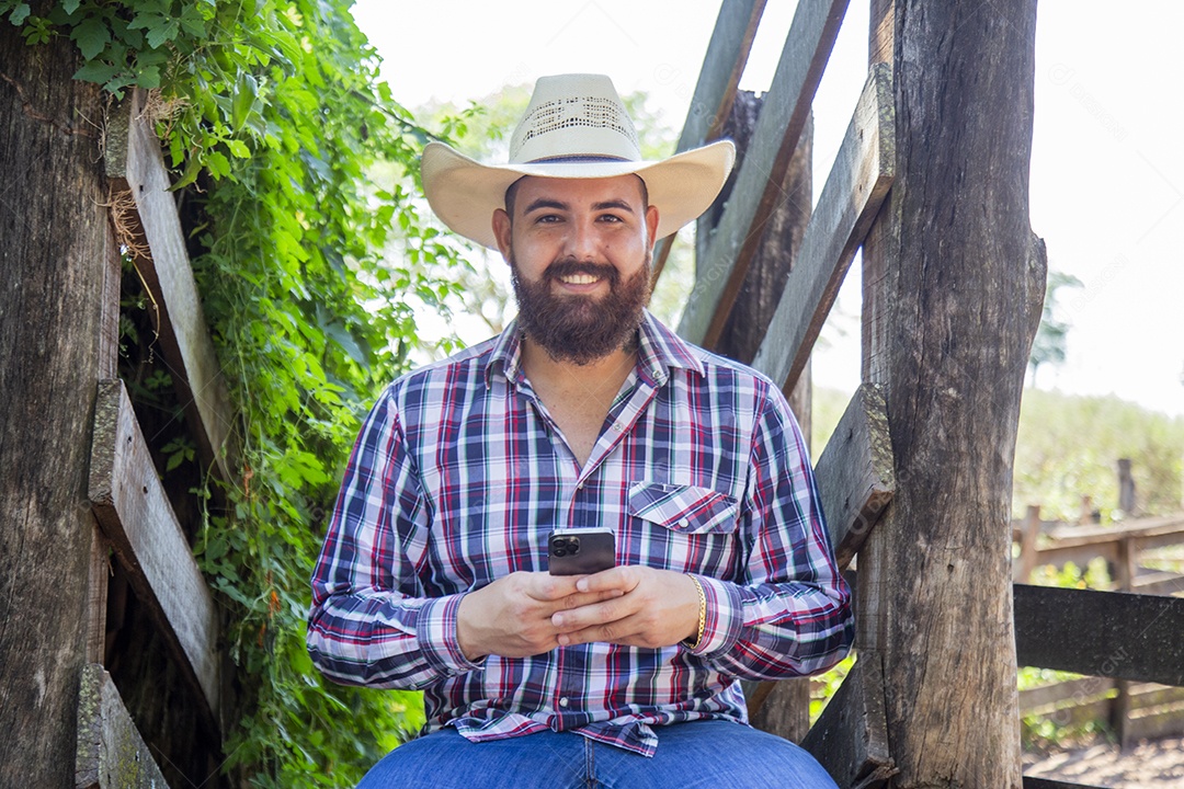 Homem jovem fazendeiro sobre fazenda segurando celular smartphone