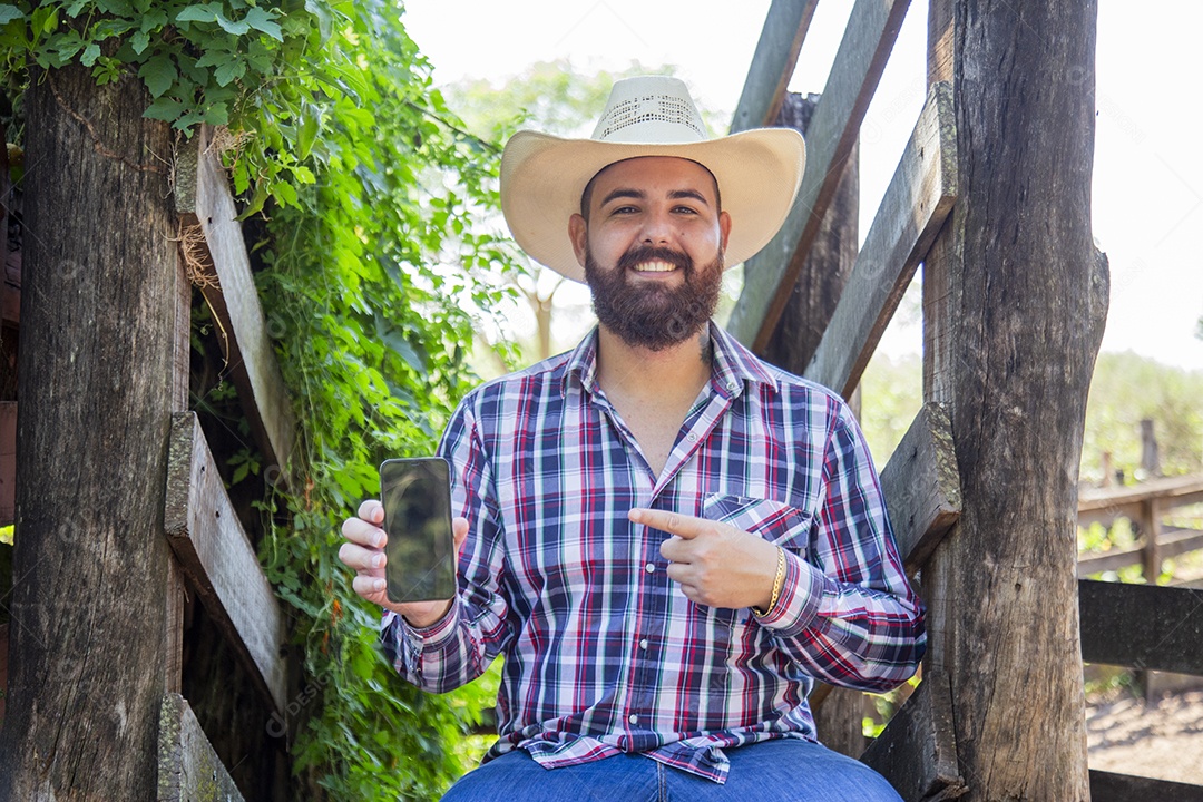 Homem jovem fazendeiro sobre fazenda segurando celular smartphone
