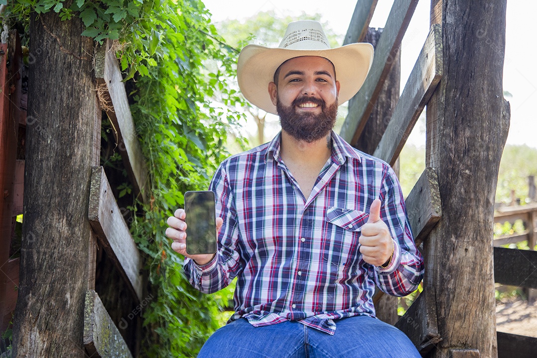 Homem jovem fazendeiro sobre fazenda segurando celular smartphone