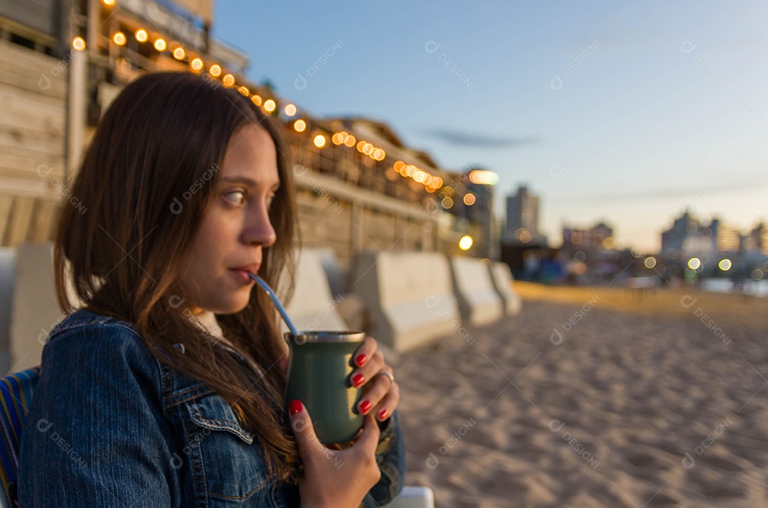 Uma mulher linda bebendo chimarrão na beira da praia