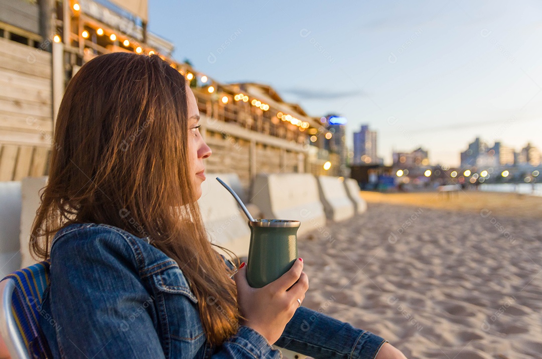 Uma bela mulher tomando chimarrão na beira da praia