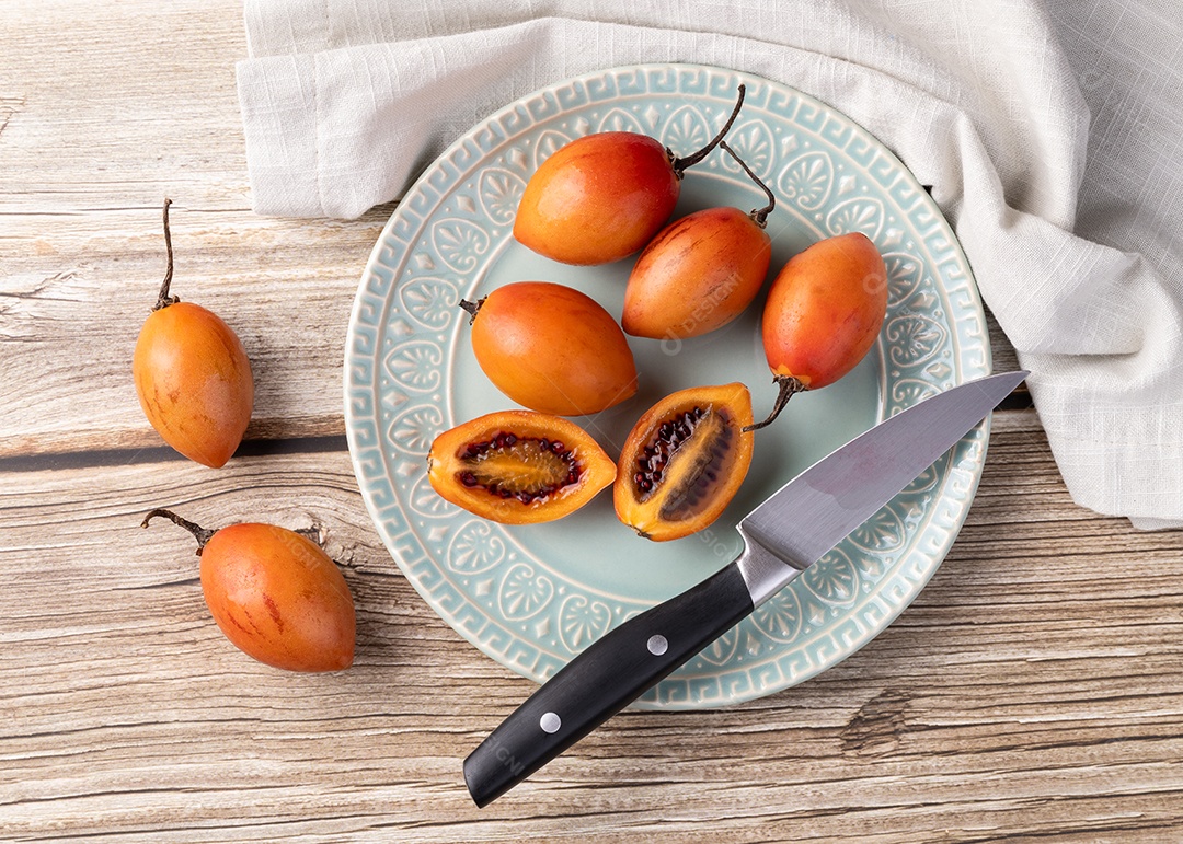 Prato com tamirillos encima sobre a mesa ao lado faca e frutos