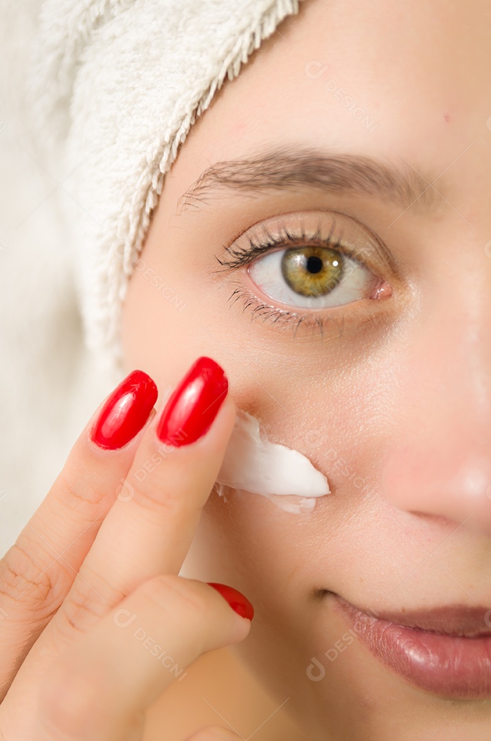 Jovem garota de olhos claros passando creme em seu rosto